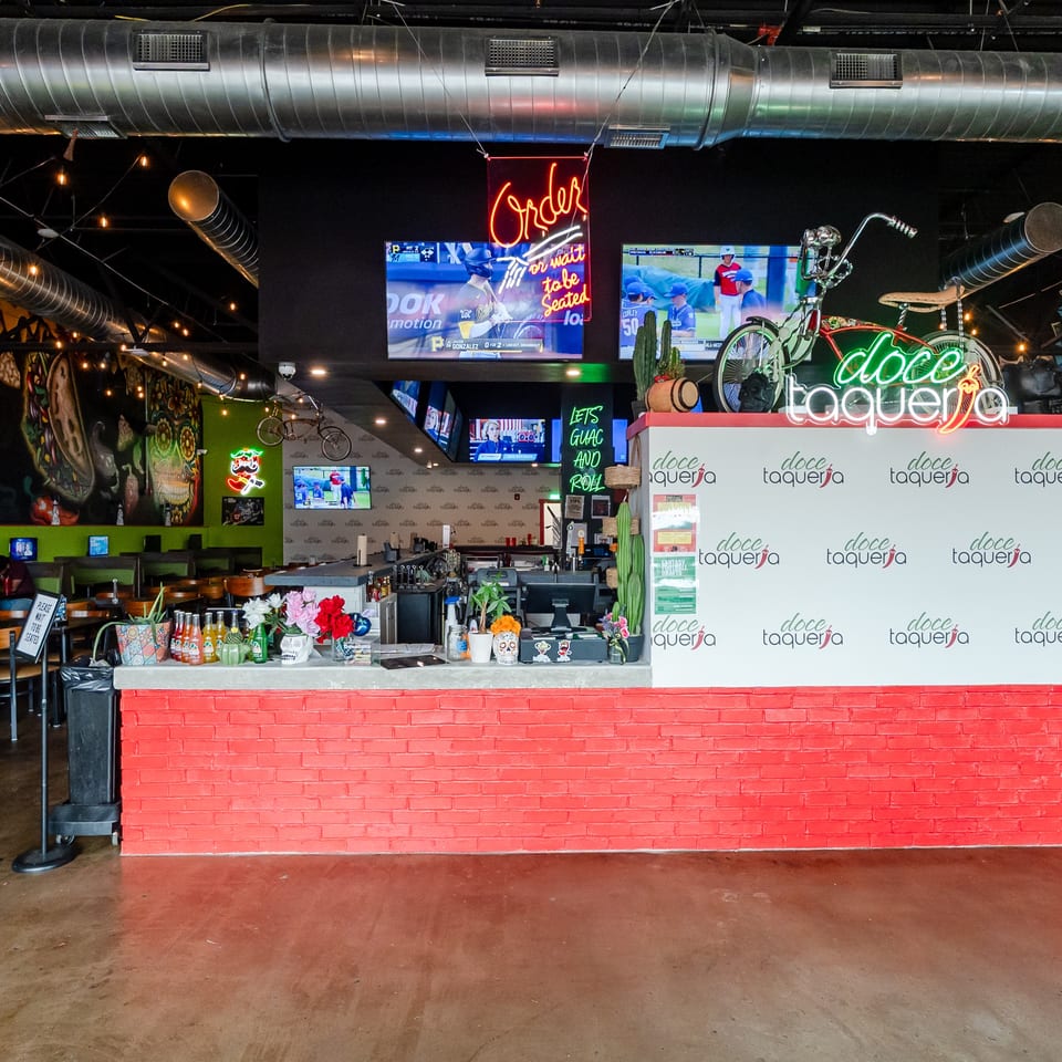 Vibrant interior of Doce Taqueria, featuring a red brick counter, neon signs, and colorful murals.