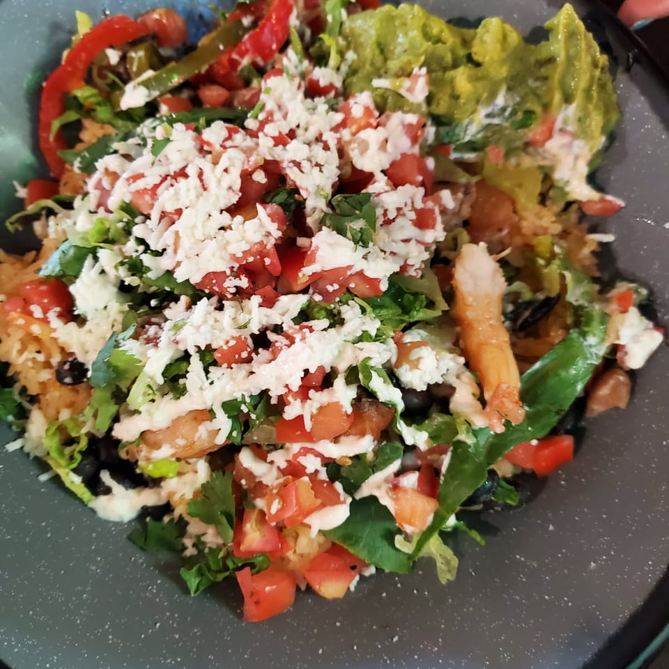 Colorful shrimp burrito bowl with rice, black beans, fresh vegetables, guacamole, and crumbled cheese.
