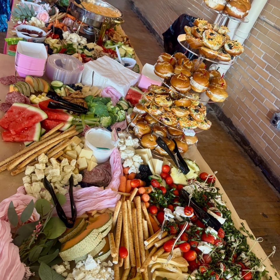 Lavish buffet spread featuring charcuterie, cheeses, fruit, vegetables, dips, and tiers of assorted sliders.