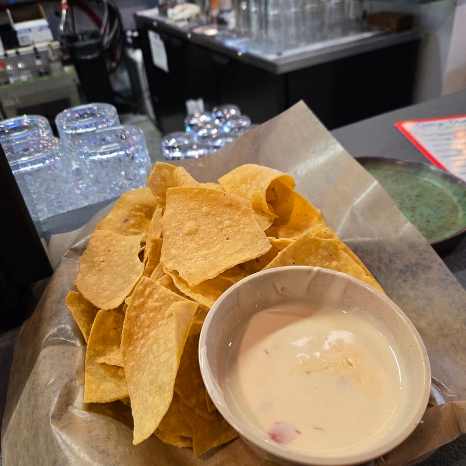 Golden tortilla chips and a bowl of creamy queso dip on a table in a bar.