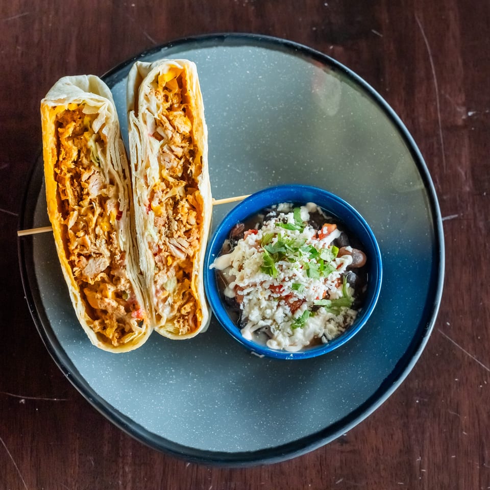 Two chicken burritos cut in half with a side of black bean salad on a dark plate.